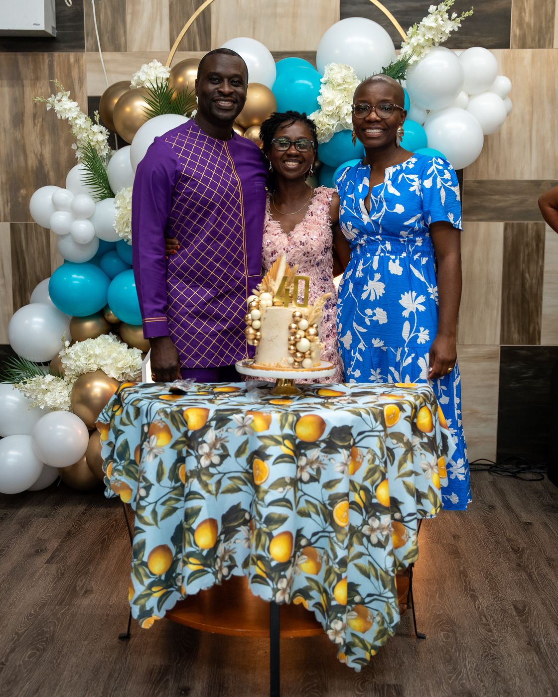 Hilda with a guest in purple and a guest in a blue floral dress by the cake