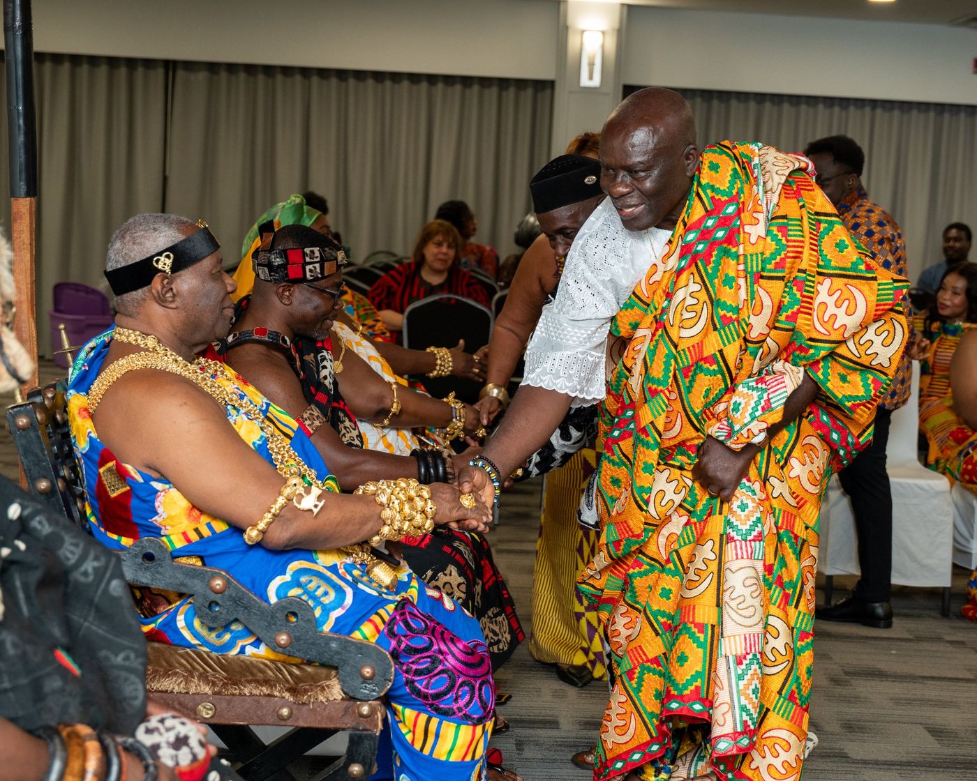 A guest in kente bows to greet a seated chief