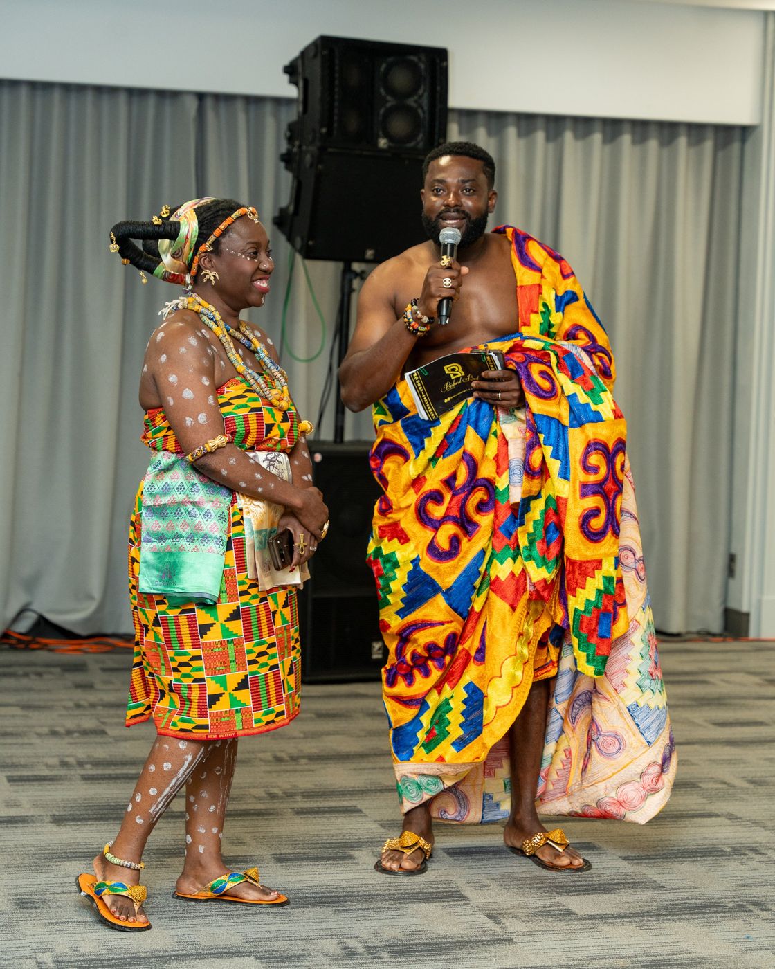 A woman in kente with white body paint beside the MC in kente cloth