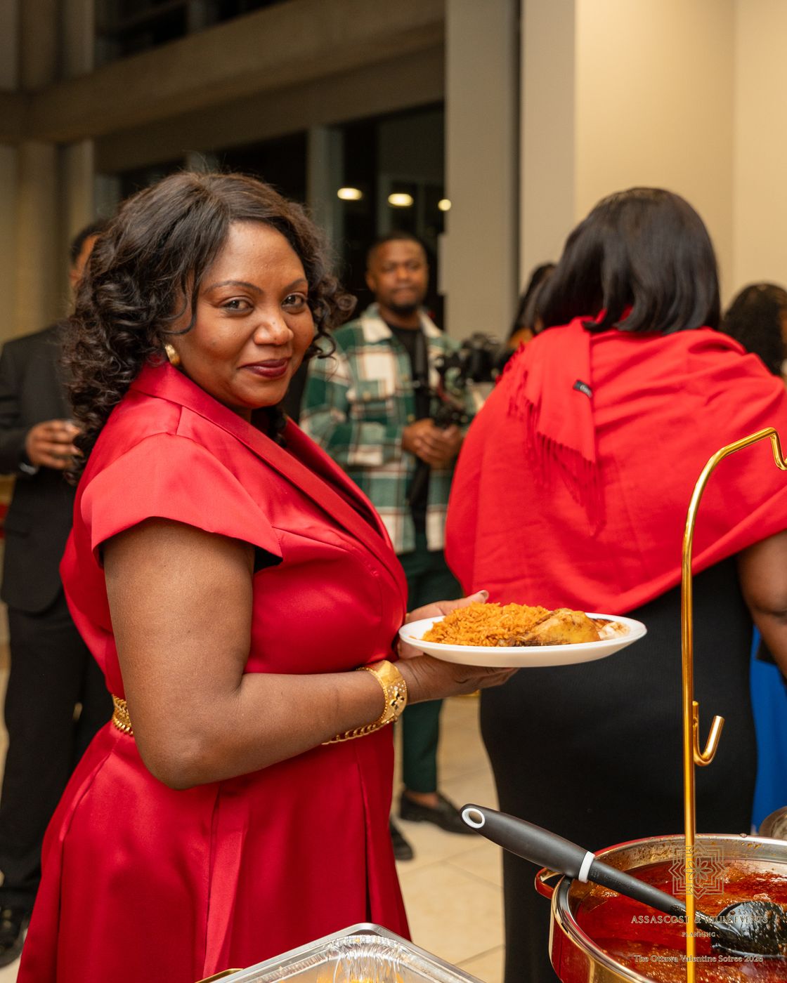 A guest in a red dress holds a plate of jollof rice and chicken
